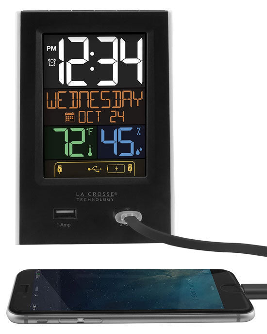 An alarm clock charging station with a color weather station display, featuring two USB charging ports. The time is shown in a large digital format with indoor temperature and humidity readings.