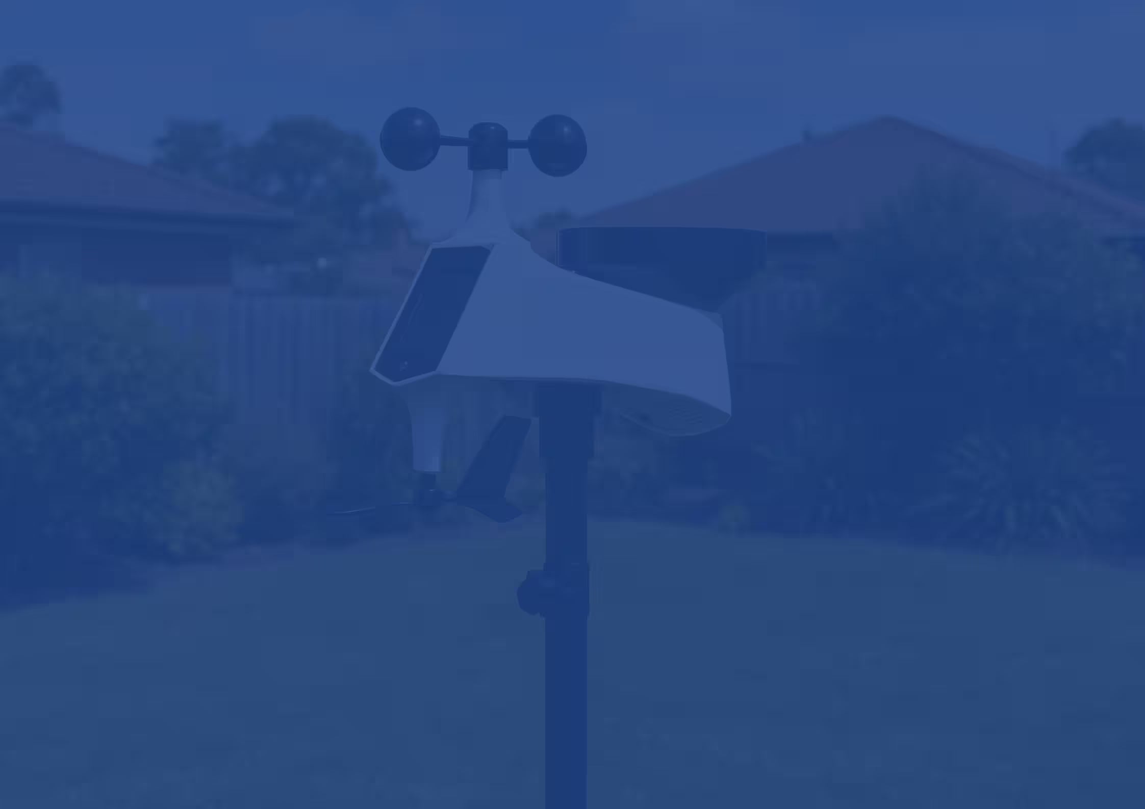 An anemometer on a pole with houses and trees in the background